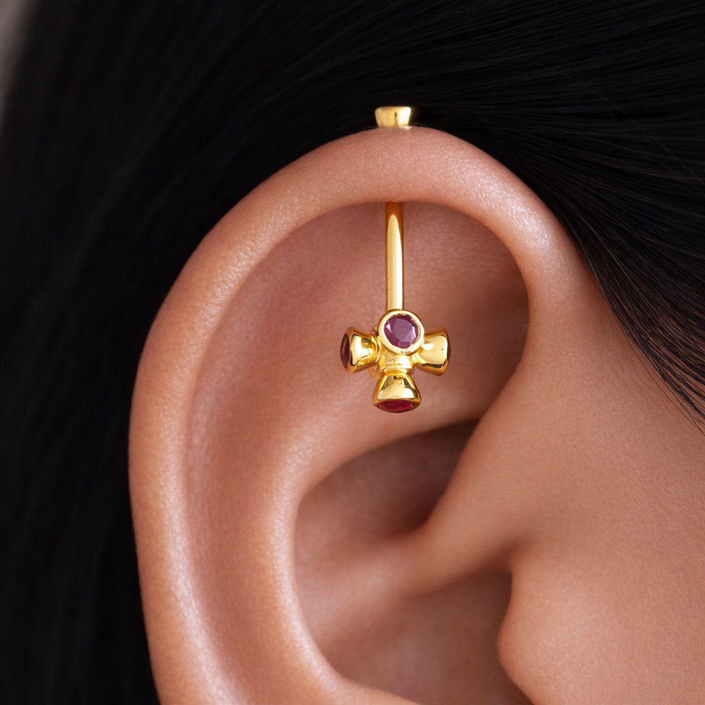 Gold earring with a red gemstone worn in an ear against a dark background